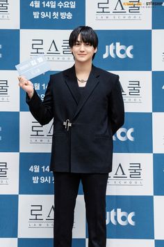 a male in a black suit is holding up a piece of paper and posing for the camera