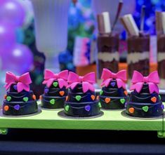 small cakes decorated with bows and hearts are on a green tray in front of other desserts