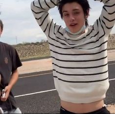 two young men standing next to each other on the side of a road with their hands behind their head