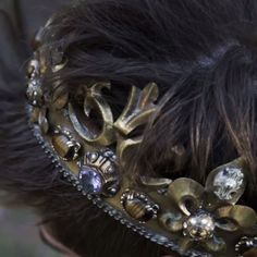 the back of a woman's head wearing a gold and silver hair piece with jewels on it