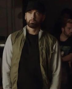 a man with a beard standing in front of a mirror wearing a black shirt and green vest