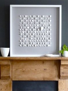 a white framed art piece sitting on top of a wooden mantle next to a potted plant