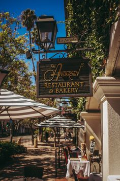 an outdoor restaurant sign hanging from the side of a building with tables and umbrellas