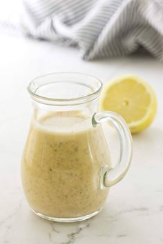 a glass pitcher filled with salad dressing next to a lemon slice