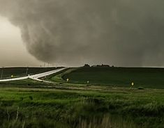 a large black cloud is in the sky over a green field