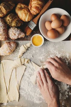 a person kneading dough on top of a table next to bread and eggs