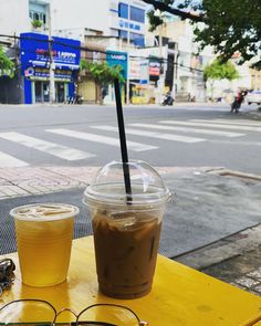 two glasses sitting on top of a yellow table next to a cup with a drink in it