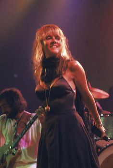 a woman in a black dress standing on stage with her guitar and singing into the microphone