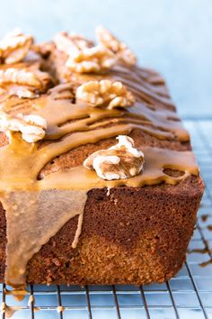 a loaf of cake with frosting and walnuts on top sitting on a cooling rack