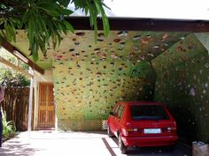 a red car is parked in front of a house with a decorative wall behind it