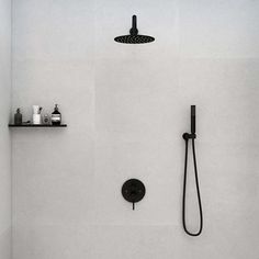 the shower head is black and there are soaps on the shelf above it, along with other bathroom items