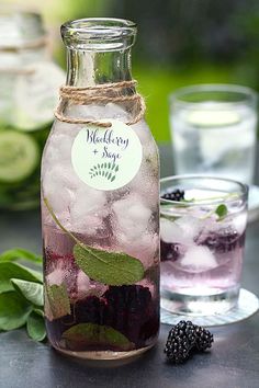 a bottle filled with ice and blackberries on top of a table next to glasses