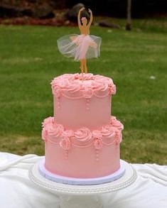 a pink cake with a ballerina figure on top and flowers in the bottom tier