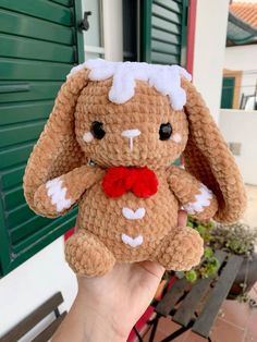 a hand holding a small stuffed animal with a red bow on it's head