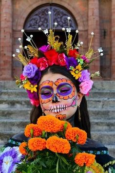 a woman with painted face and flowers on her head is standing in front of a building