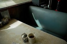 two coffee cups sitting on top of a table next to a window with the blinds open