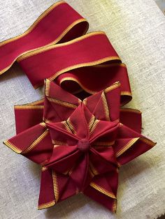 a close up of a red bow on a white cloth with gold trimmings