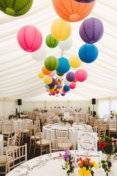 colorful paper lanterns hang from the ceiling above tables and chairs in a marquee