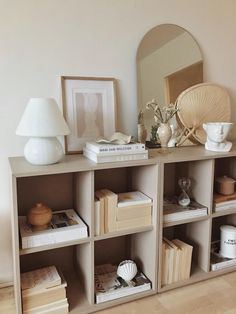 a book shelf with books, vases and other items on it in front of a mirror