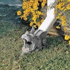 an animal statue laying on the ground next to yellow flowers and a white fence post