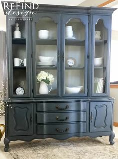 a black china cabinet with glass doors and drawers on the bottom, in front of a vase