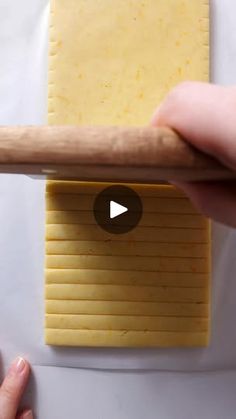 a person holding a wooden stick over a piece of cheese on top of a white surface