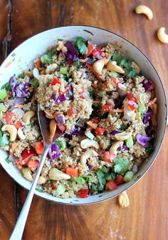 a bowl filled with rice and vegetables on top of a wooden table next to cashews