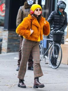 a woman wearing a fur coat and headphones walking down the street while talking on her cell phone