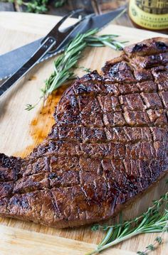 a steak on a cutting board with a knife next to it and some rosemary sprigs