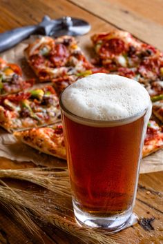 a glass of beer sitting on top of a wooden table next to slices of pizza