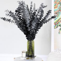 a vase filled with lots of black flowers on top of a white table next to a painting