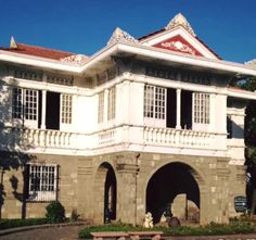 a large white building with many windows and balconies on the top floor, in front of a tree