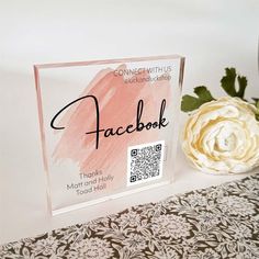 a clear acrylic sign sitting on top of a table next to a flower