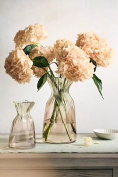 two vases with flowers in them sitting on a table next to a plate and bowl