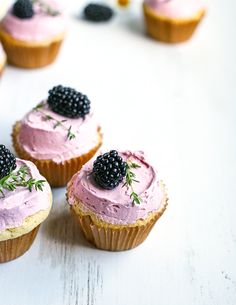 three cupcakes with pink frosting and blackberries on top are arranged next to each other