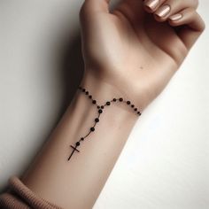 a woman's arm with a cross tattoo on it and a black beaded bracelet