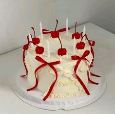 a white cake with red ribbons and cherries on it