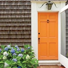 an orange front door with blue hydrangeas in the foreground