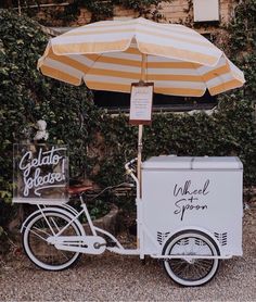 an ice cream cart is parked under an umbrella