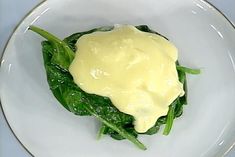 a white plate topped with spinach covered in sauce