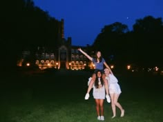 three girls posing in front of a large building at night