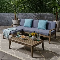 a couch and coffee table on a patio with potted plants in the back ground