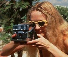 a woman with long blonde hair and sunglasses holding a camera in front of her face