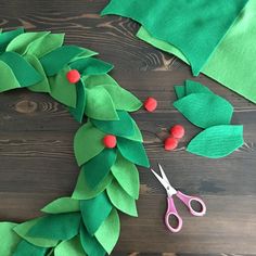 a christmas wreath made out of green felt and red berries on top of a wooden table