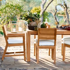 a wooden table with white chairs and plants on top of it in front of trees