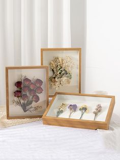 three framed pictures with flowers in them on a white tableclothed surface next to a window