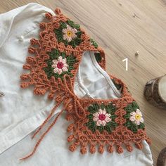 an orange crocheted top with flowers on the front and back, sitting on a wooden floor