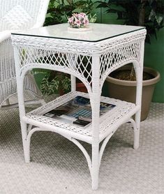 white wicker side table with glass top and magazine holder on the ground next to potted plant