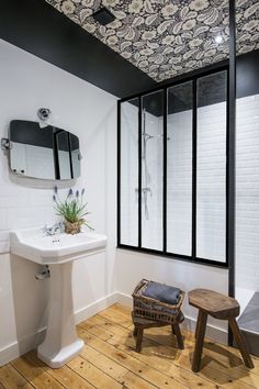 a white sink sitting under a bathroom mirror next to a wooden stool and window in front of it