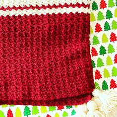 a red crocheted blanket sitting on top of a white table next to christmas trees